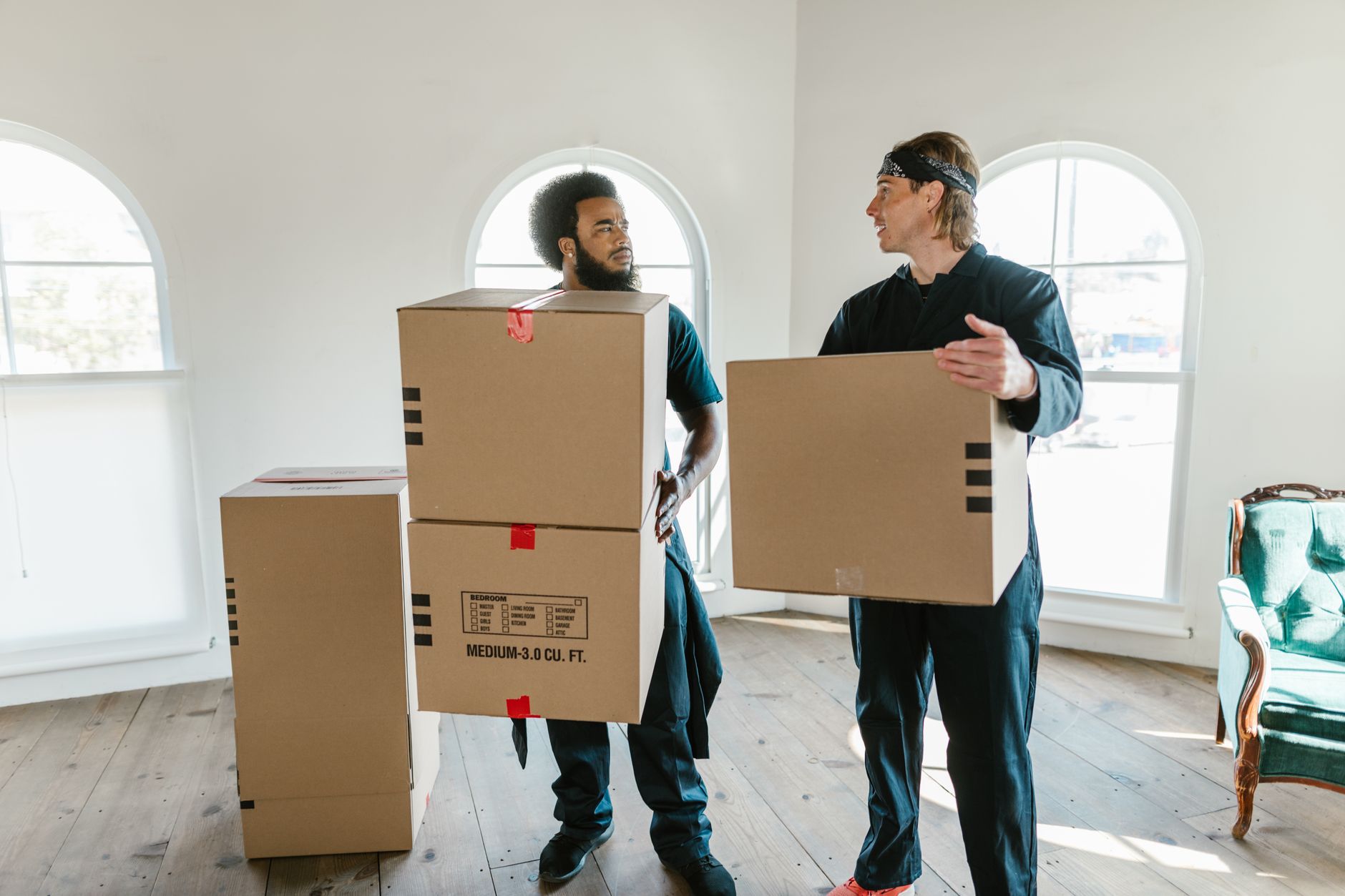 Two professional movers carrying cardboard boxes inside a bright room during a residential move