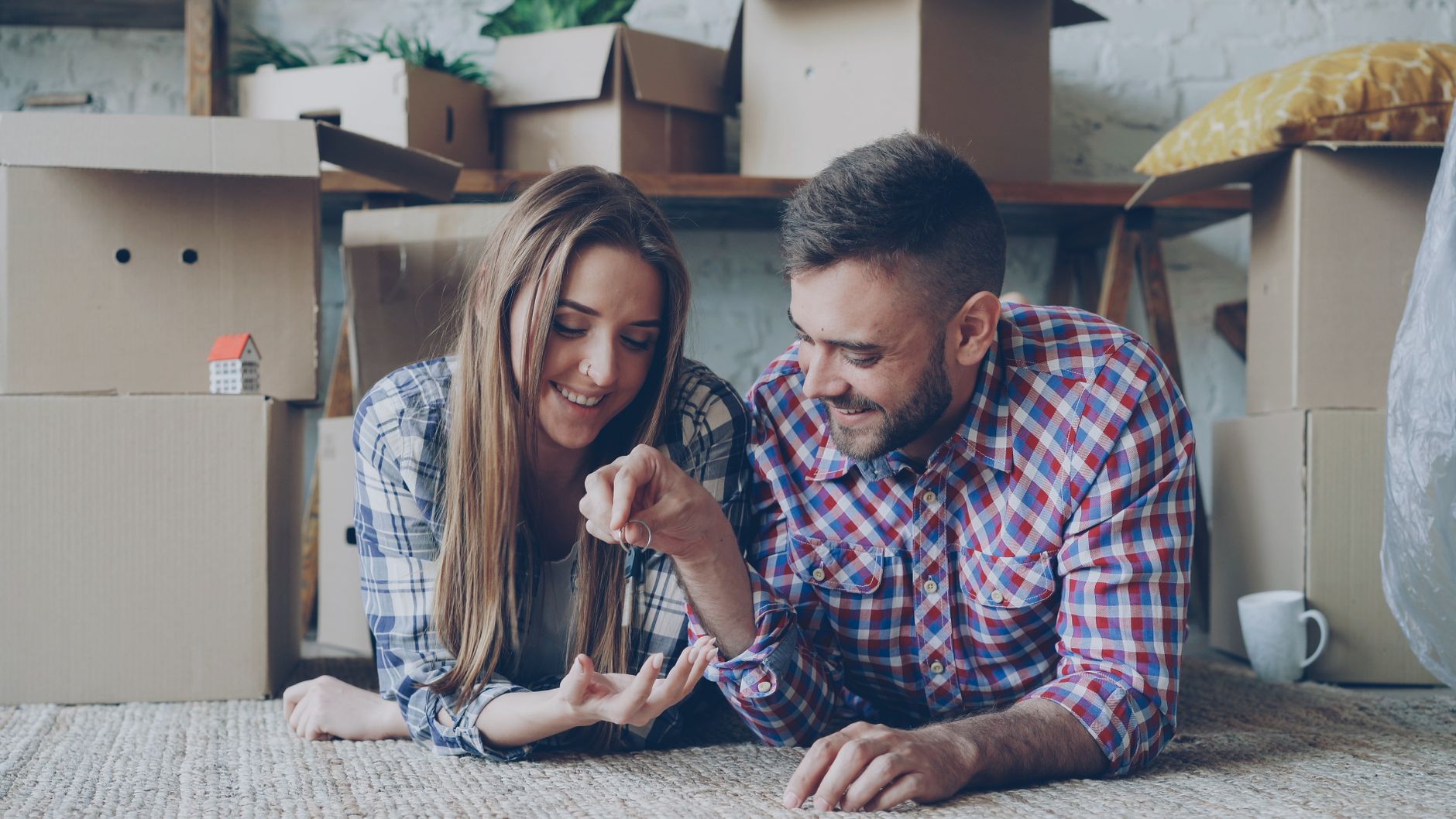 Happy couple holding keys to their new home surrounded by moving boxes